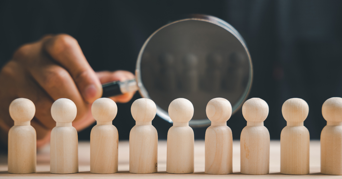 A magnifying glass focuses on a row of small wooden pegs that represent the population